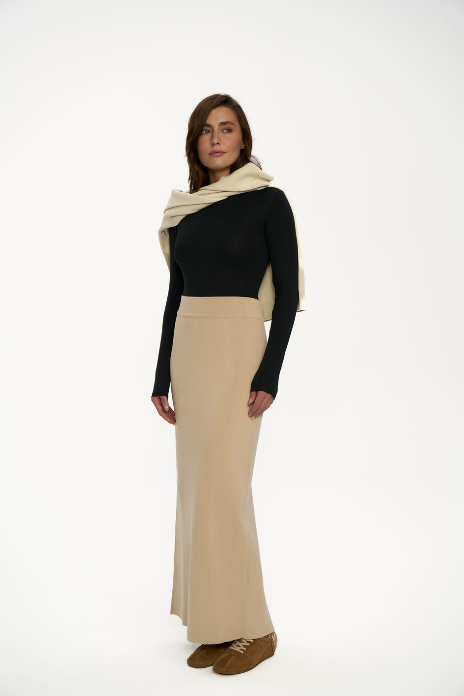 Beige long knit maxi skirt styled with black fitted top and light sweater over shoulders on model, three-quarter view – Inner Tiger