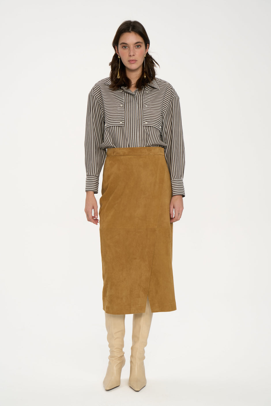 Woman wearing a striped shirt, brown suede skirt, and beige boots on a white background
