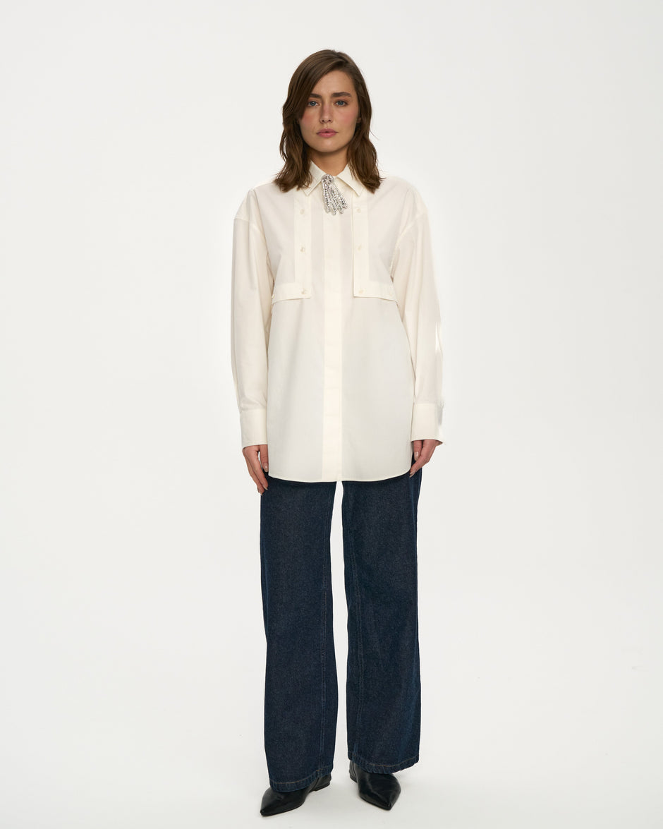 White cotton breastfeeding-friendly shirt with mother-of-pearl buttons and detachable brooch styled with dark indigo wide-leg jeans, full length front view – Inner Tiger
