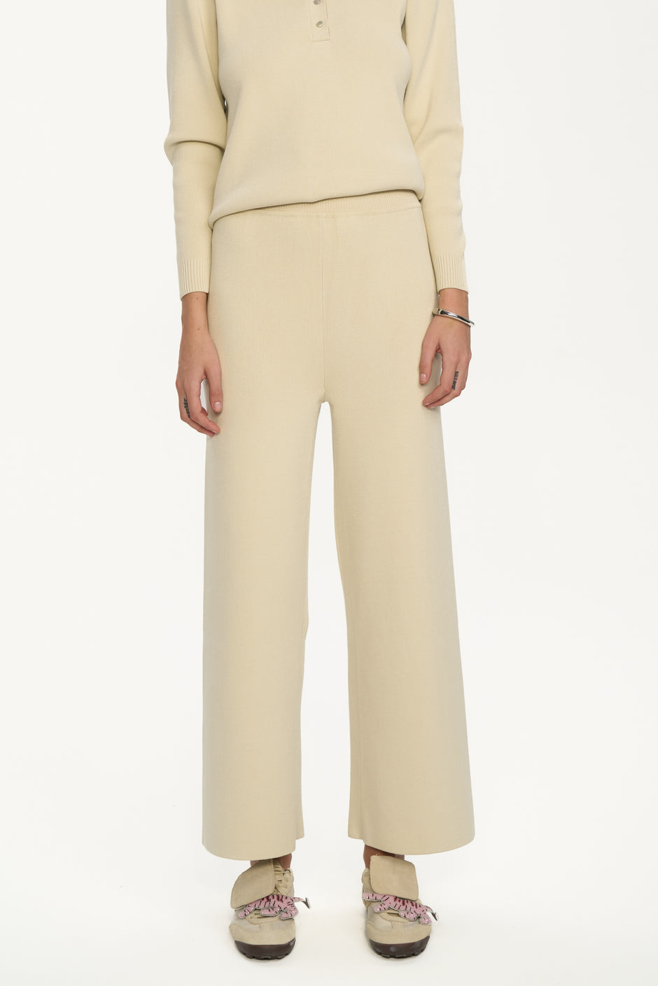 Person wearing a beige outfit with wide-leg pants on a white background