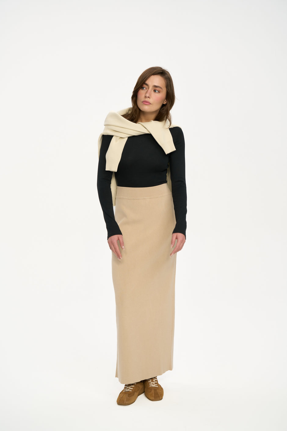 Woman wearing a black top, beige skirt, and cream scarf on a white background