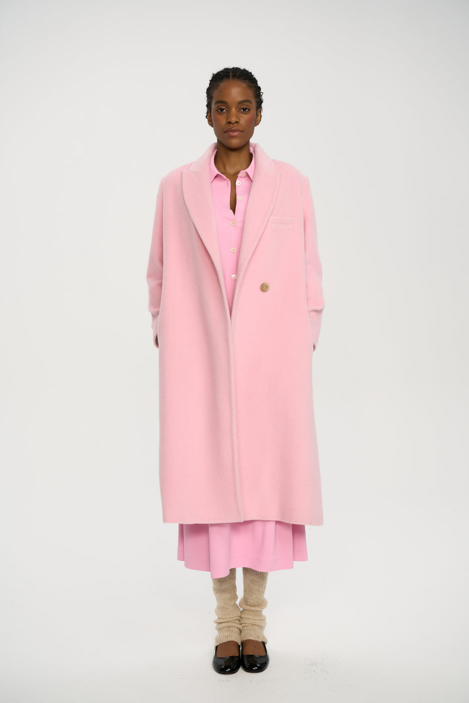 Person wearing a long pink coat over a pink dress on a white background