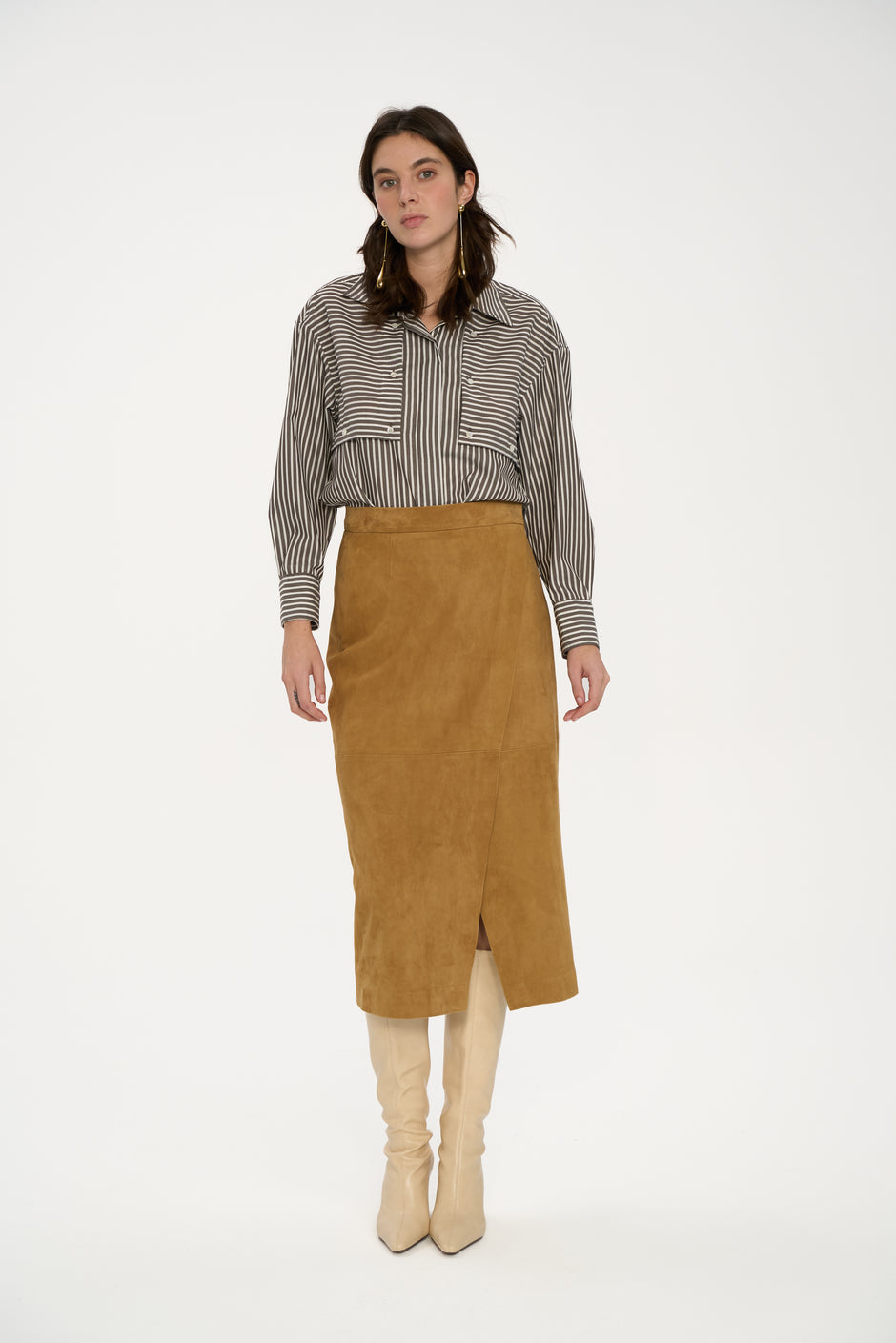 Woman wearing a striped shirt, brown suede skirt, and beige boots on a white background