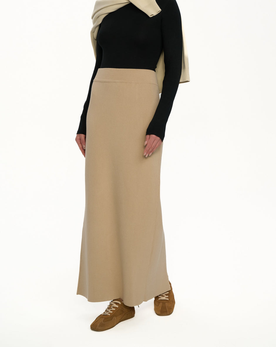 Woman wearing a black top, beige skirt, and brown shoes on a white background