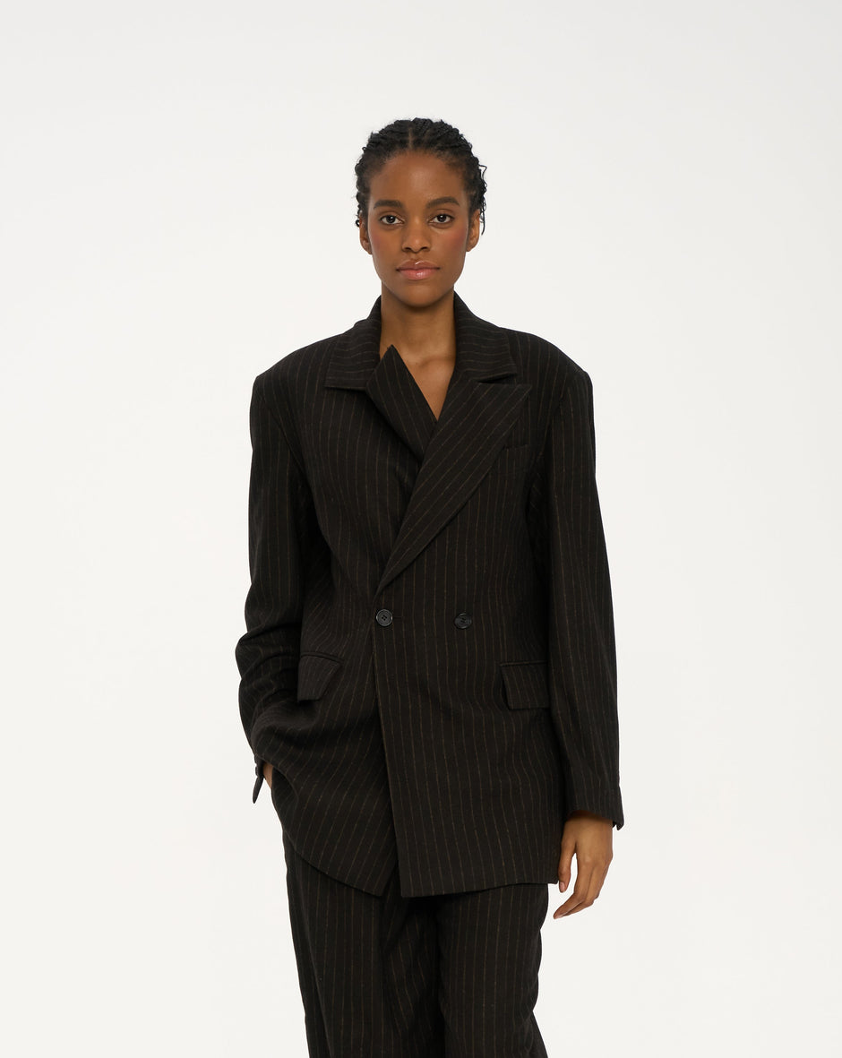 Model wearing chocolate brown pinstripe tailored jacket and matching trousers, minimal styling, front full body shot – Inner Tiger