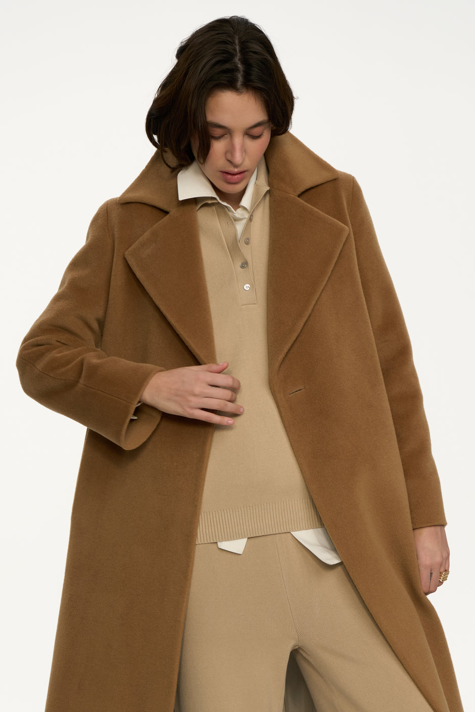 Detail of camel wool wrap coat with wide lapels styled over beige knit polo and knit trousers – Inner Tiger