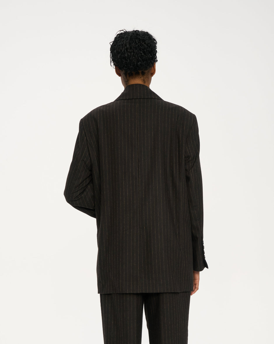 Back view of chocolate brown pinstripe double-breasted blazer with relaxed straight trousers, worn with sneakers – Inner Tiger
