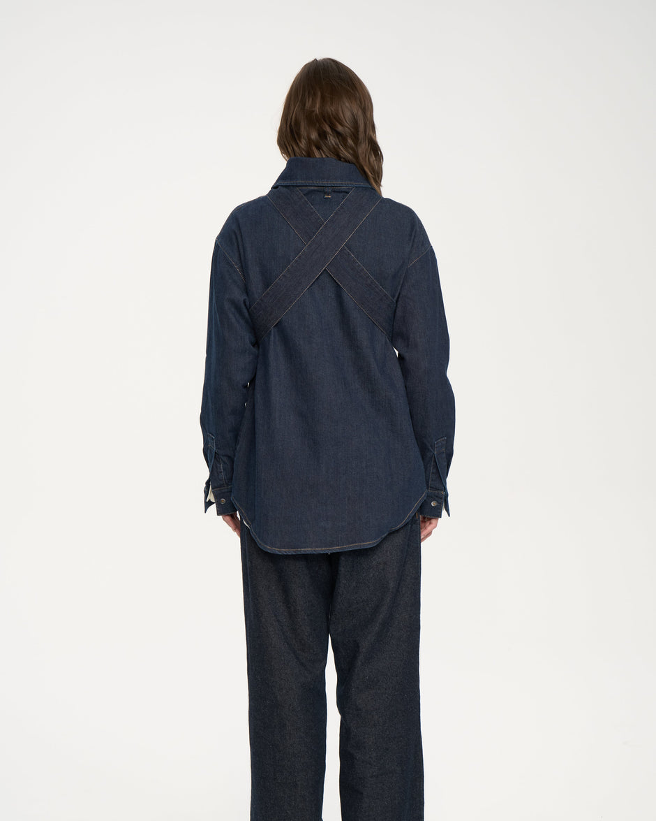 Model wearing indigo denim bow overshirt cinched at the waist over cream shirt and dark indigo jeans – Inner Tiger