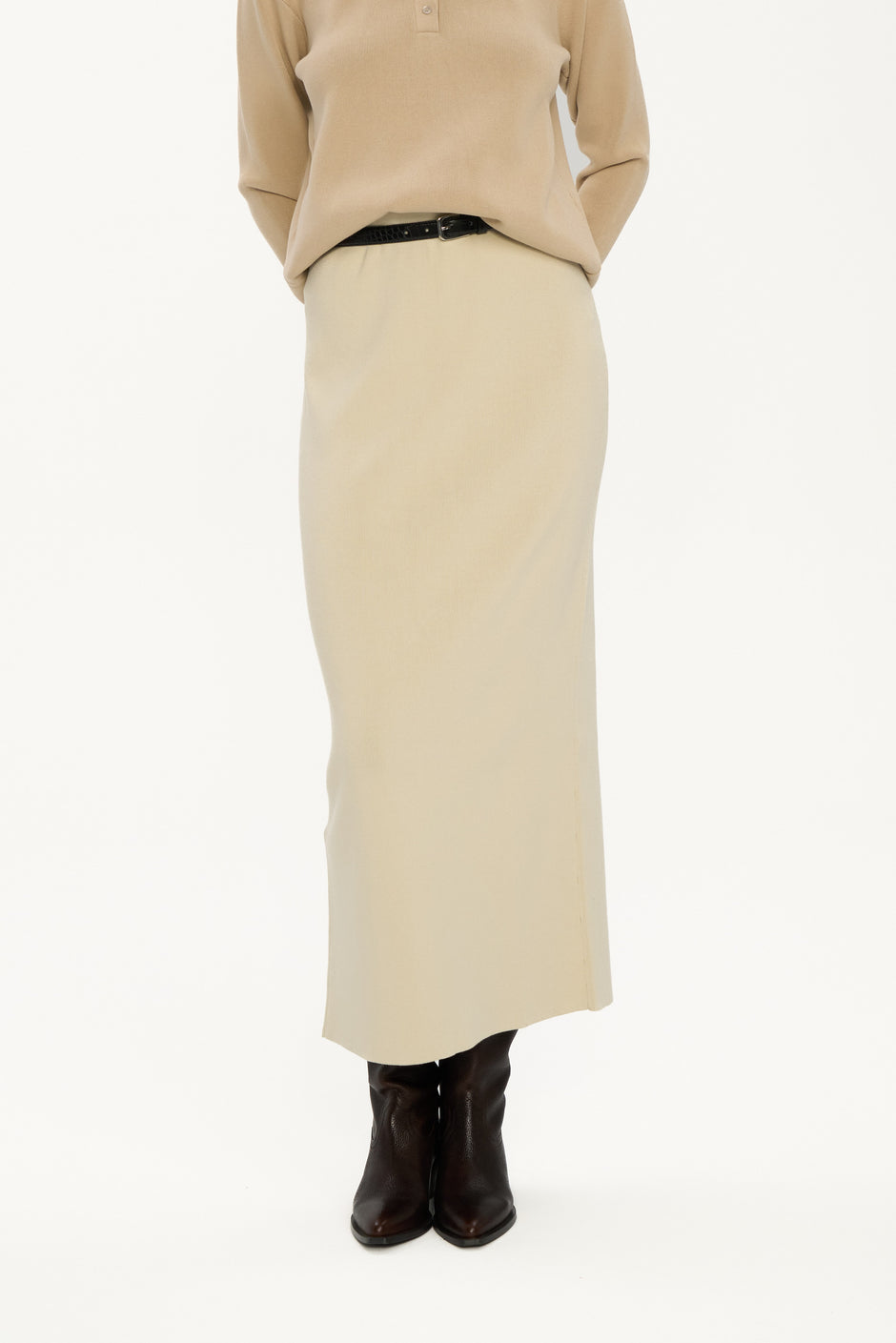 Person wearing a beige sweater and long skirt with brown boots on a white background
